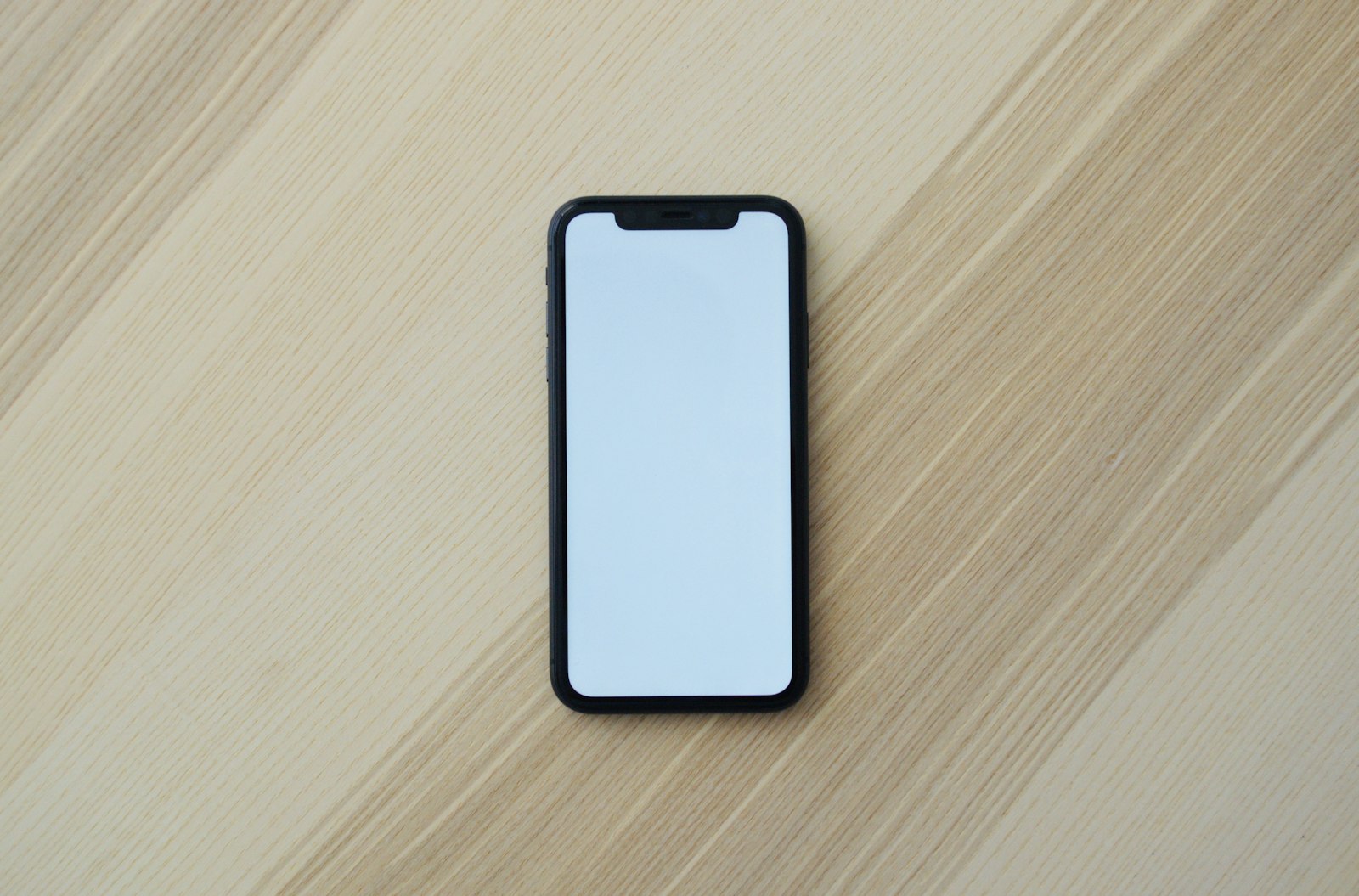 A phone with a blank screen resting on a wooden desk