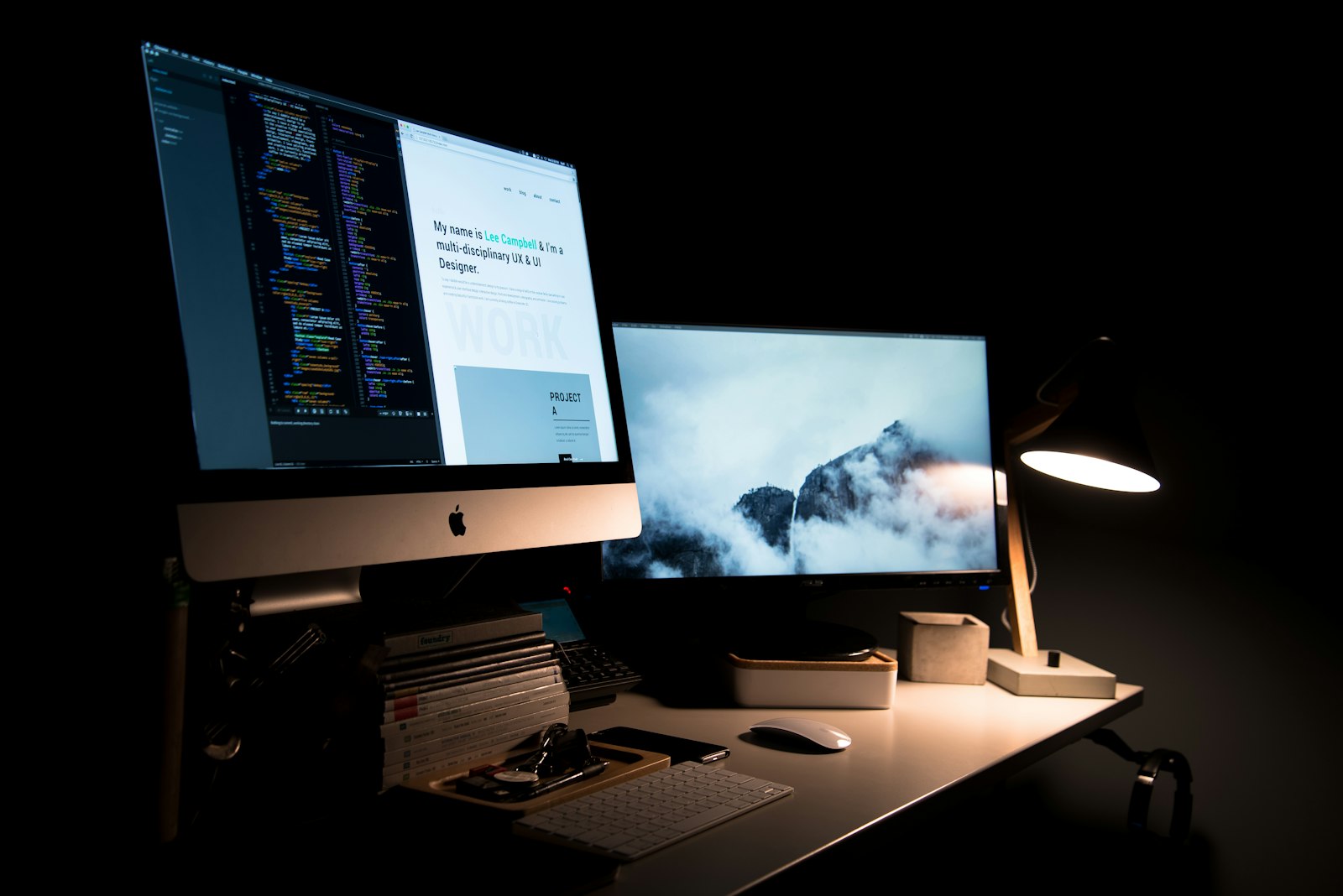 Two monitors showing code and a website design